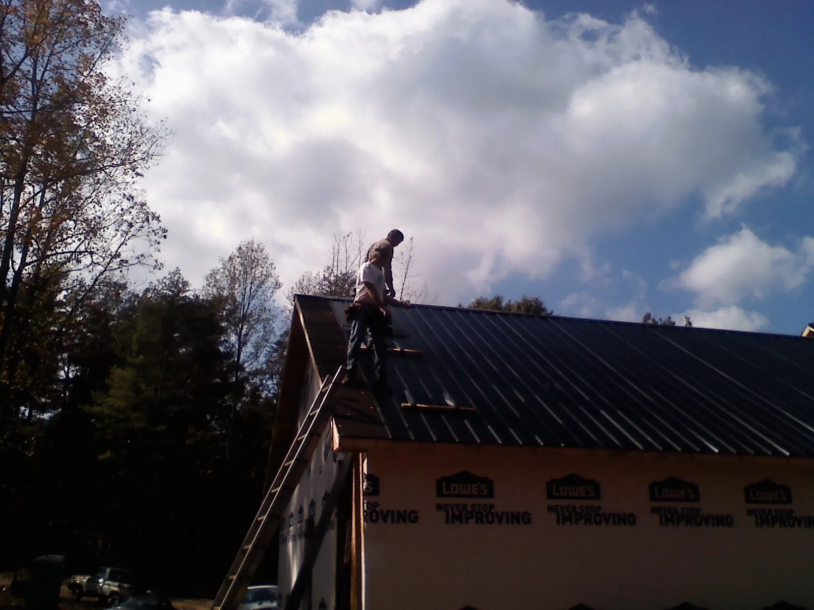 Roofer fastening dark metal panels high against a cloudy sky, from a Roof Inspection job in Snoqualmie Pass